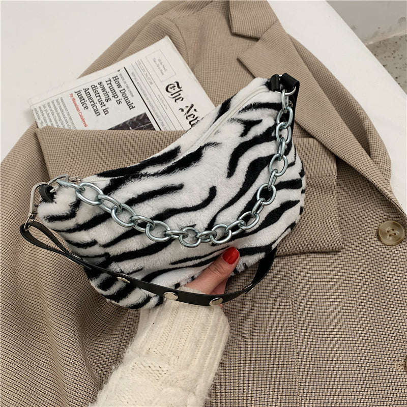 Zebra print bag with chain detail held by a person wearing a beige coat.