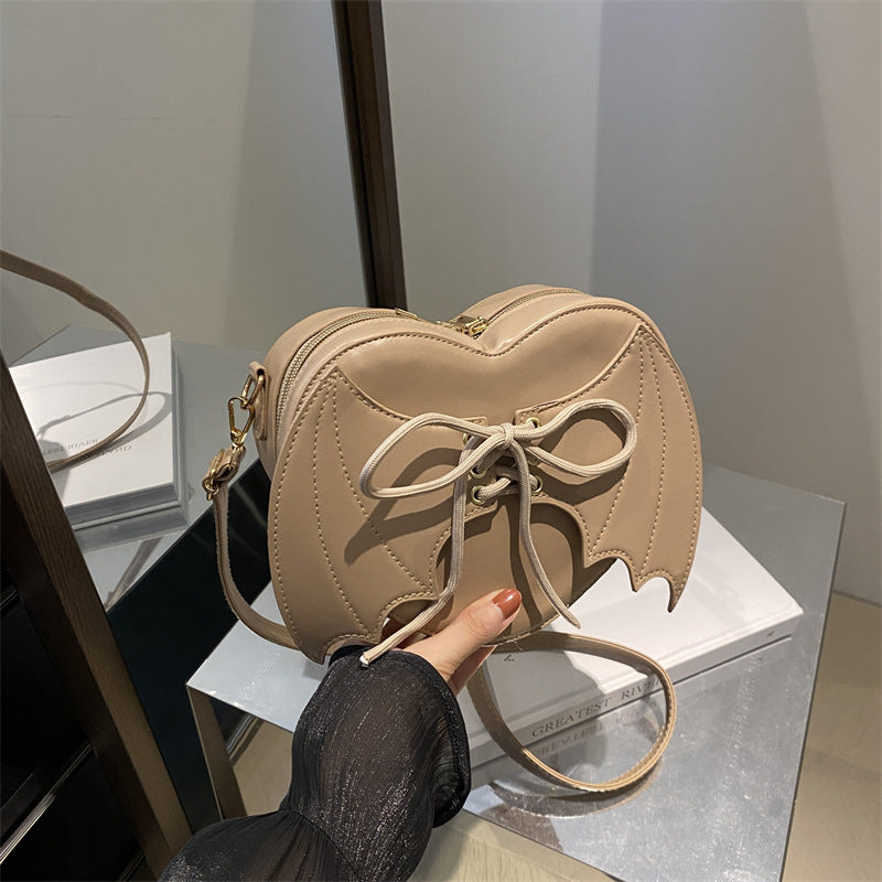 Beige handbag with bow detail held by a person on a reflective surface.