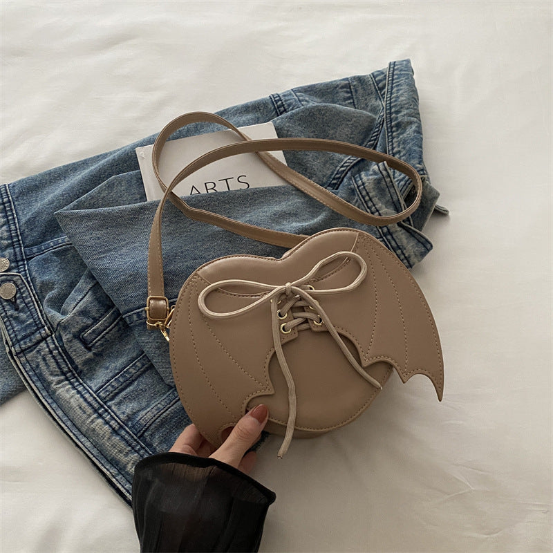 Beige heart-shaped bag with a bow held by a hand on a white surface with denim jeans.