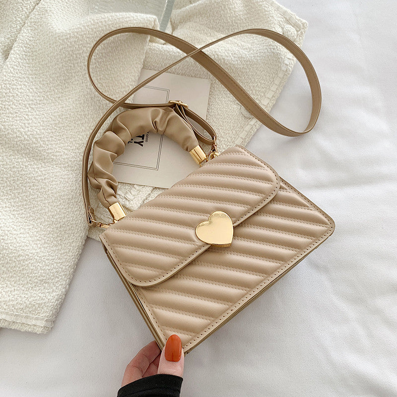 Beige quilted handbag with a heart-shaped gold clasp on a light background