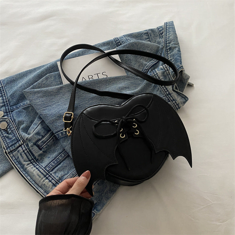 Black bat-shaped handbag held over a denim jacket on a light background
