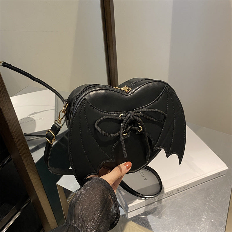 Black bat-wing shaped handbag held by a person against a neutral background
