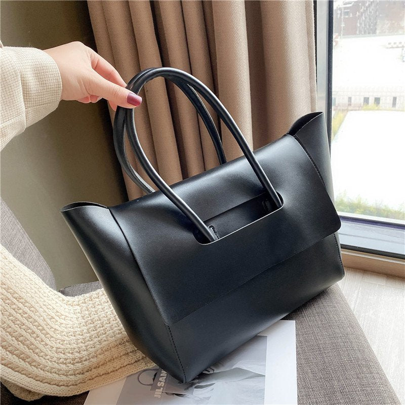 Black handbag held by a person sitting on a couch with a window and curtain in the background