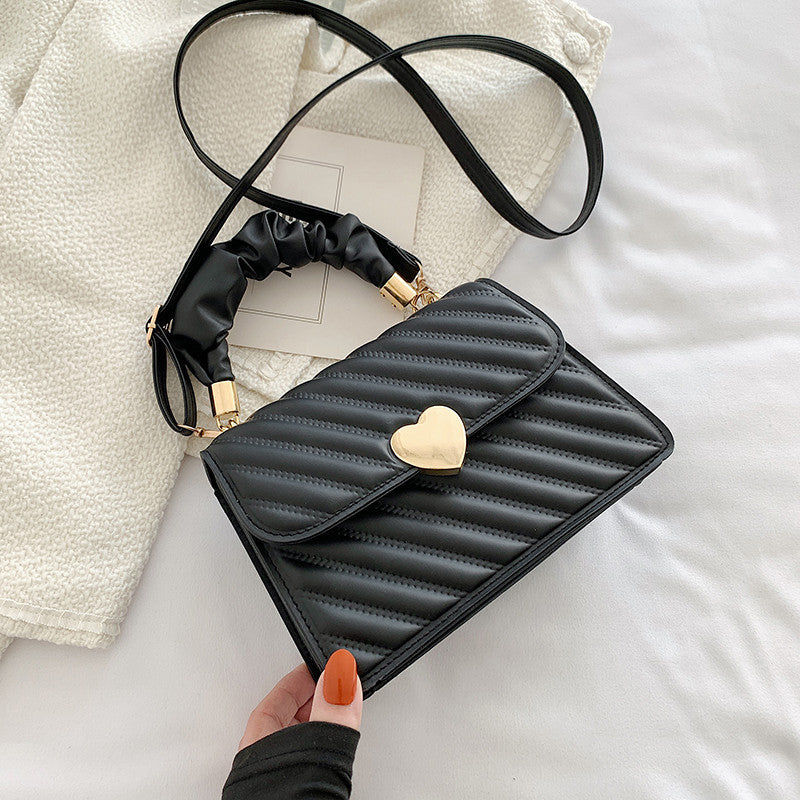 Black quilted handbag with a heart-shaped clasp held by a hand on a light background