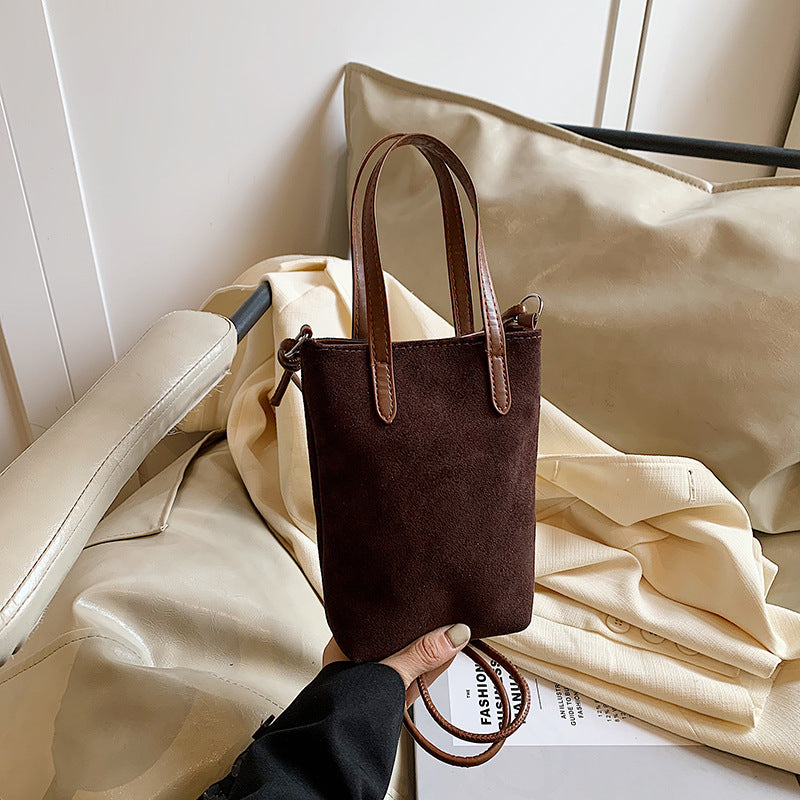 Brown handbag with leather handles held by a person on a beige surface.
