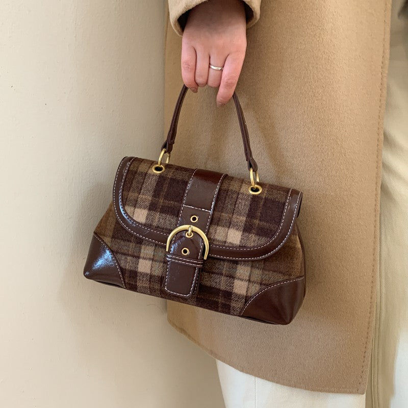 Brown plaid handbag held by a person wearing a beige coat.