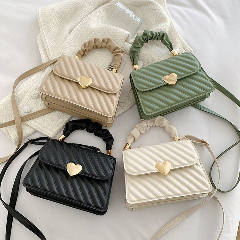 Four small handbags in beige, green, black, and white with heart-shaped clasps on a light background.