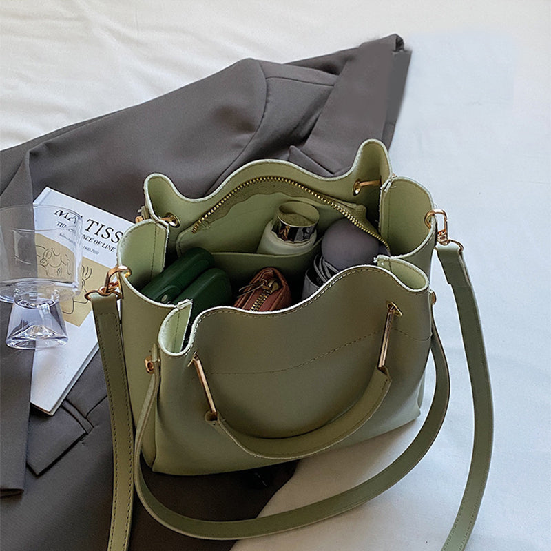 Green handbag with gold accents on a white surface with gray fabric