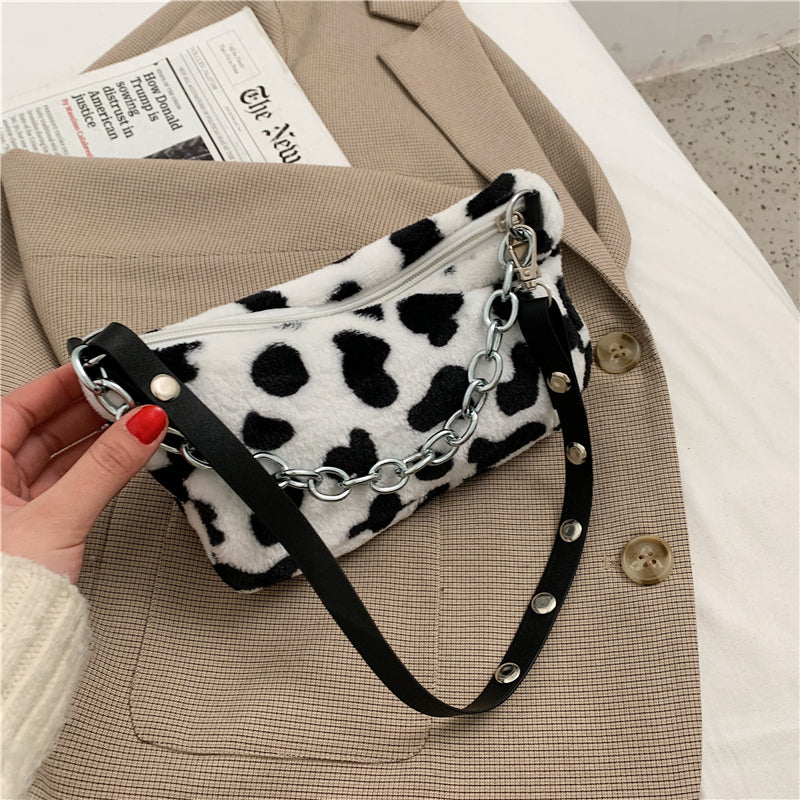 Handbag with cow print pattern held by a hand on a textured surface
