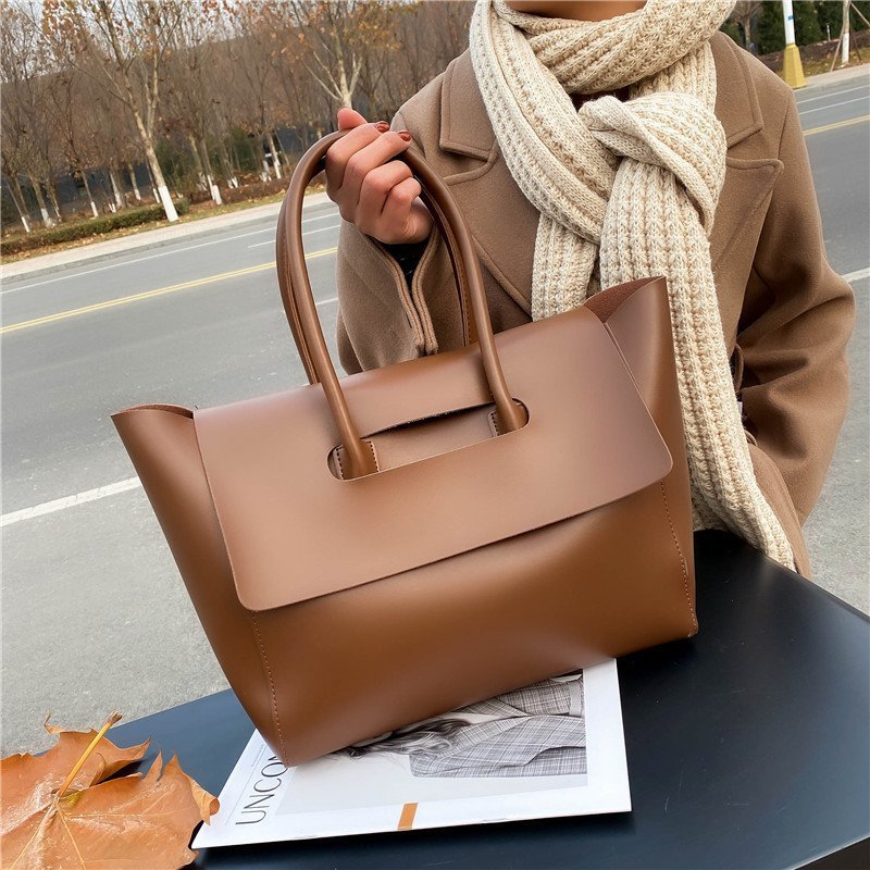 Person holding a brown handbag with a scarf and coat, standing on a road.