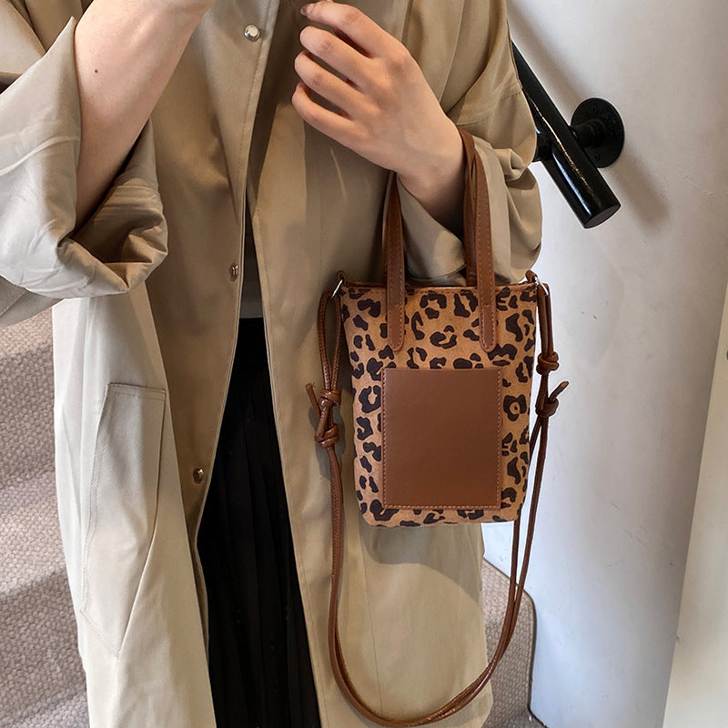 Person holding a leopard print crossbody bag with a plain background