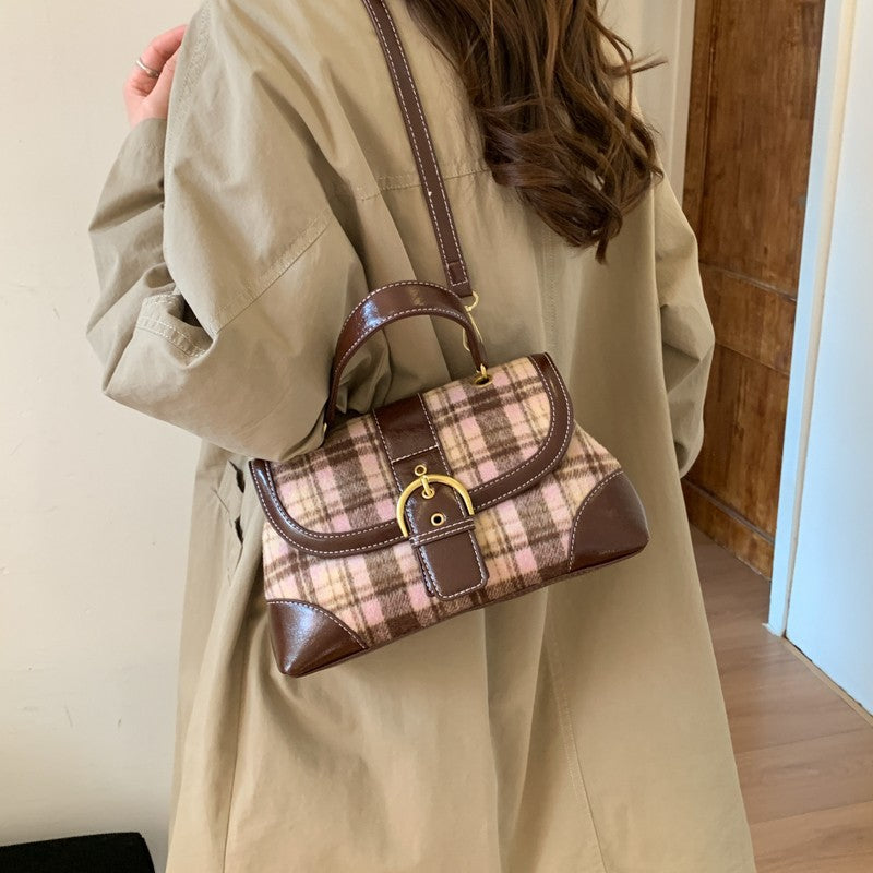 Person holding a plaid handbag with a brown leather trim against a neutral background