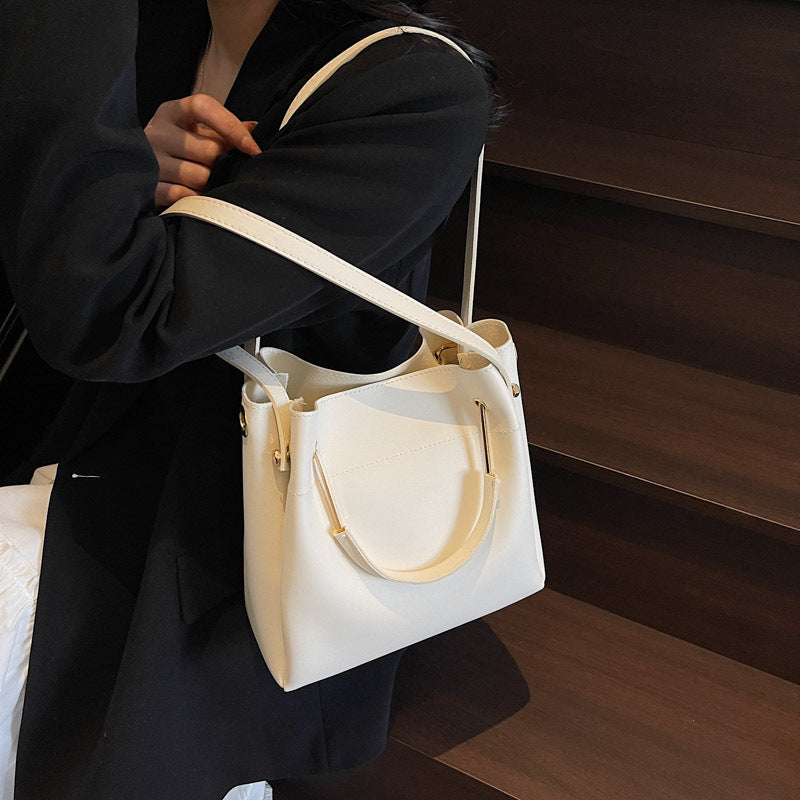 Person holding a white handbag with beige straps on a wooden floor.