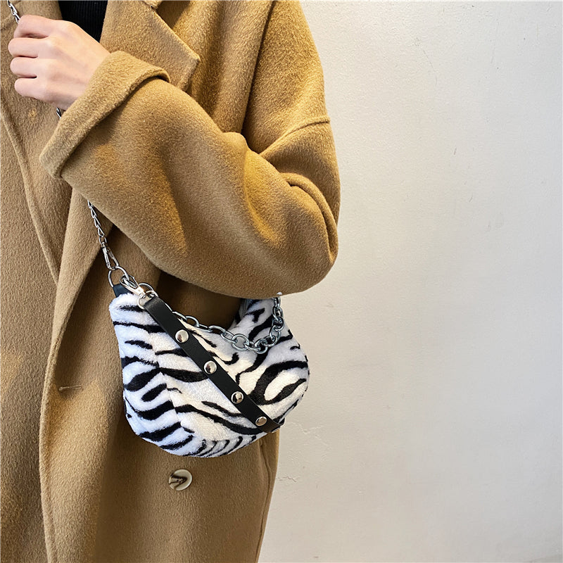 Person wearing a beige coat holding a zebra-striped handbag against a plain background