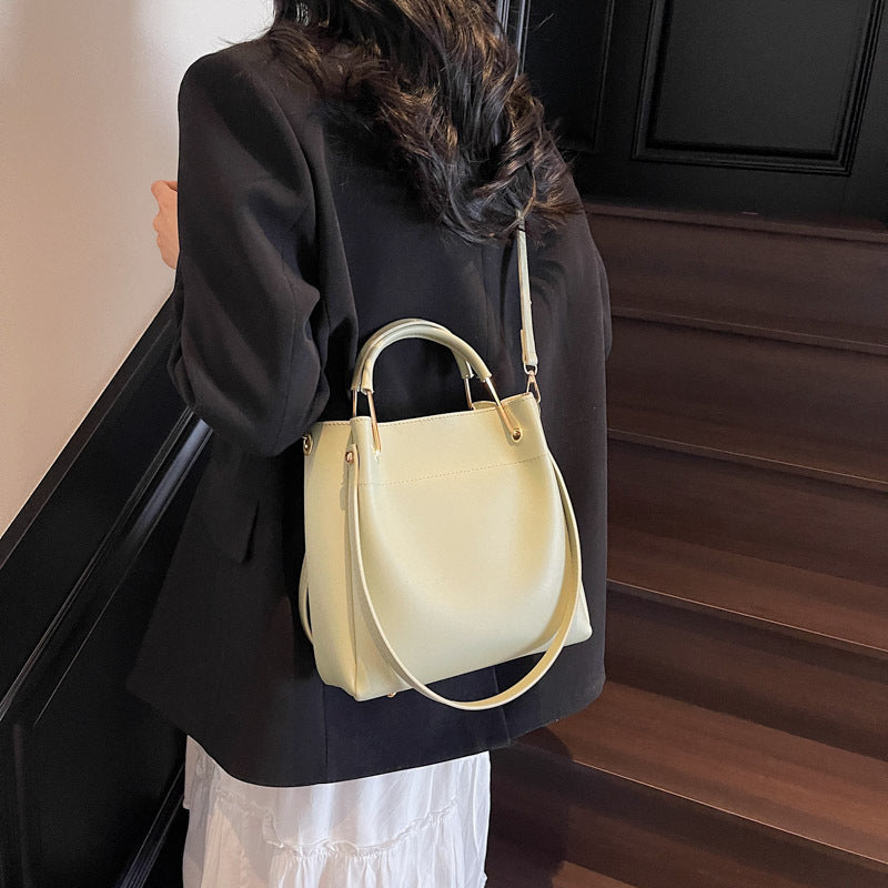 Person wearing a black blazer and white dress with a light yellow handbag on a wooden staircase.