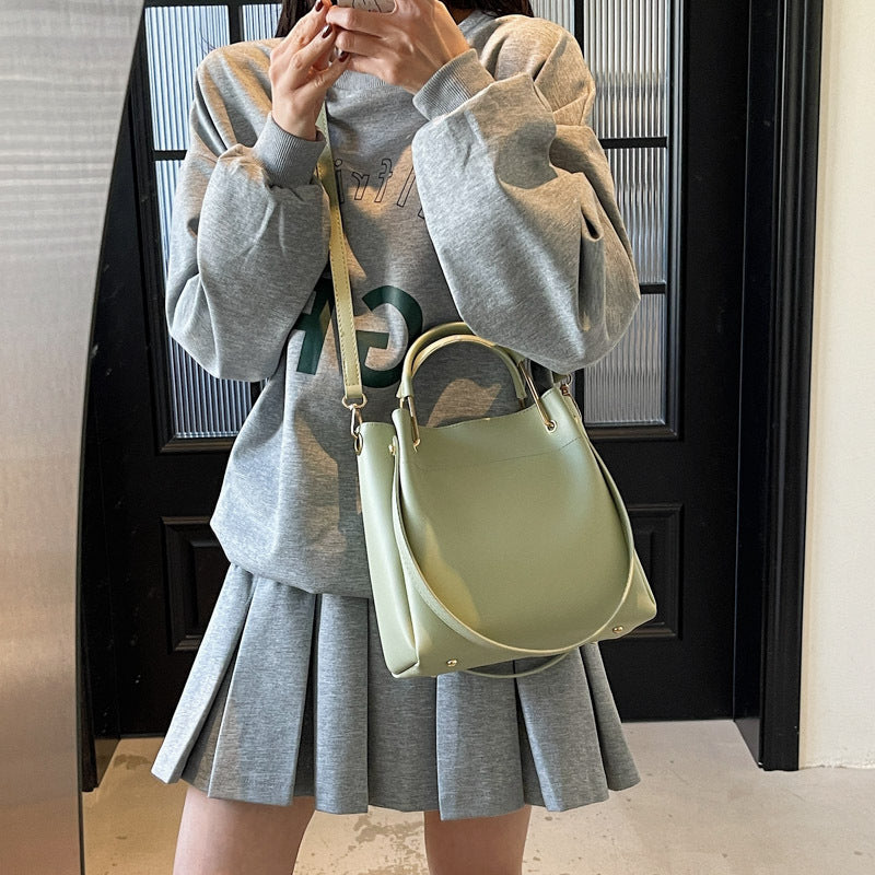 Person wearing a gray sweatshirt and pleated skirt holding a light green handbag.