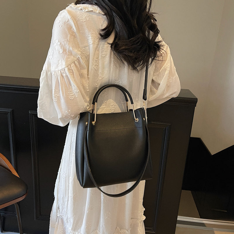 Person wearing a white dress holding a black handbag indoors.