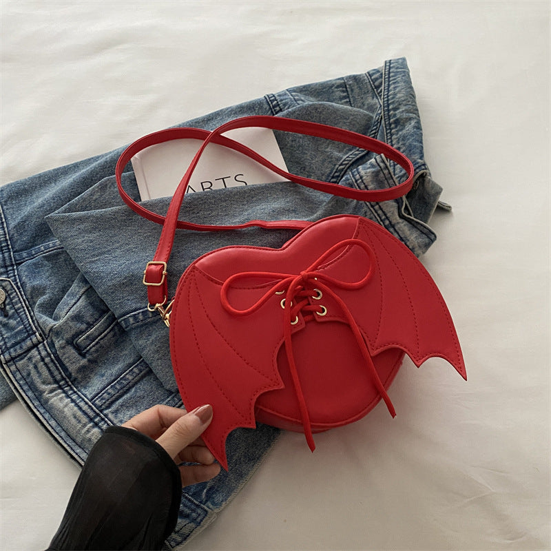 Red heart-shaped bag with wings and a bow held by a hand on a denim jacket background