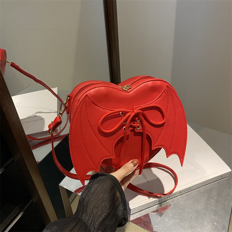 Red heart-shaped handbag with a bow held by a person, on a reflective surface.