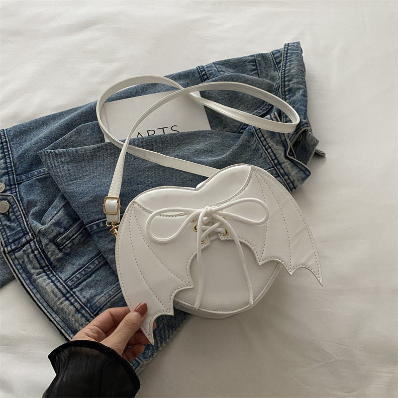 White heart-shaped bag with a bow held by a hand on a denim jacket background