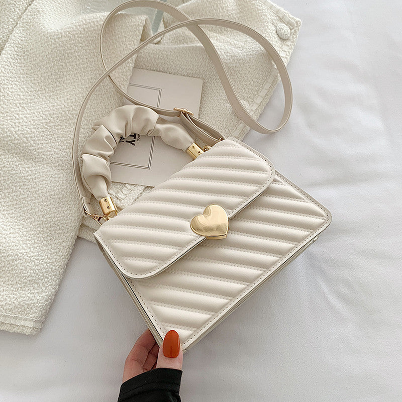 White quilted handbag with a gold heart detail held by a hand on a light background