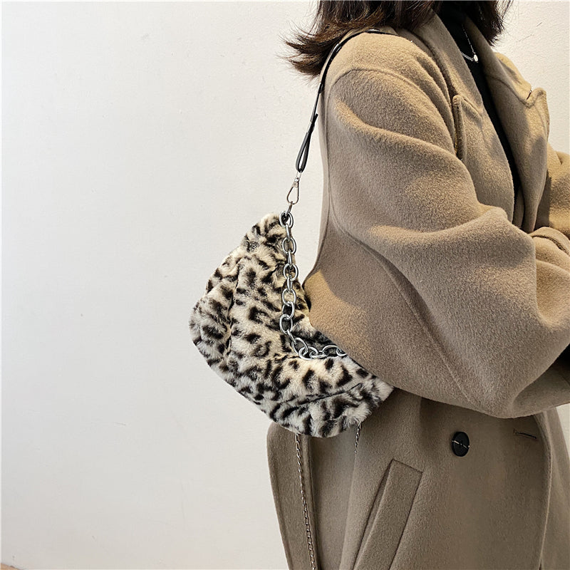 Person wearing a beige coat holding a leopard print handbag against a plain background